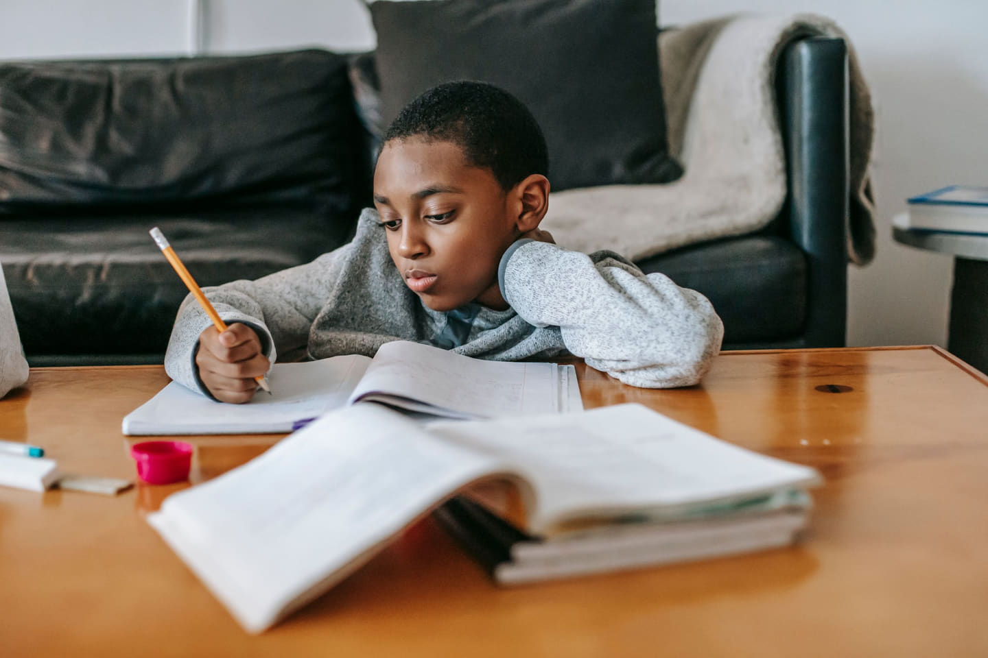 A boy part-way through a page of homework, pencil in hand, two textbooks open in front of him